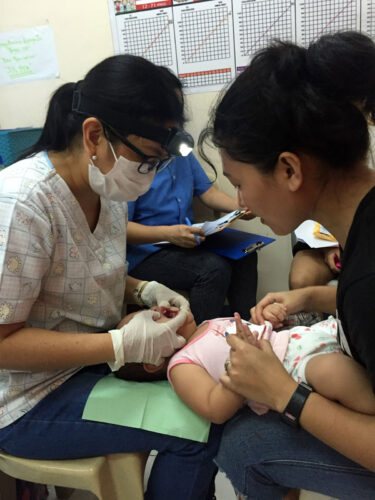 Dr. Oliveros-Villarico (left) performs an oral health exam