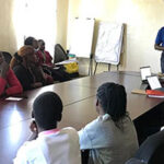 Group of eople around a table at 2025 Kisumu Clinic Feedback Meeting Kombewa